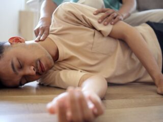 Ilustračný stock: kľačiaca osoba podkladá ležiacemu človeku hlavu zloženou bundou, civilne.